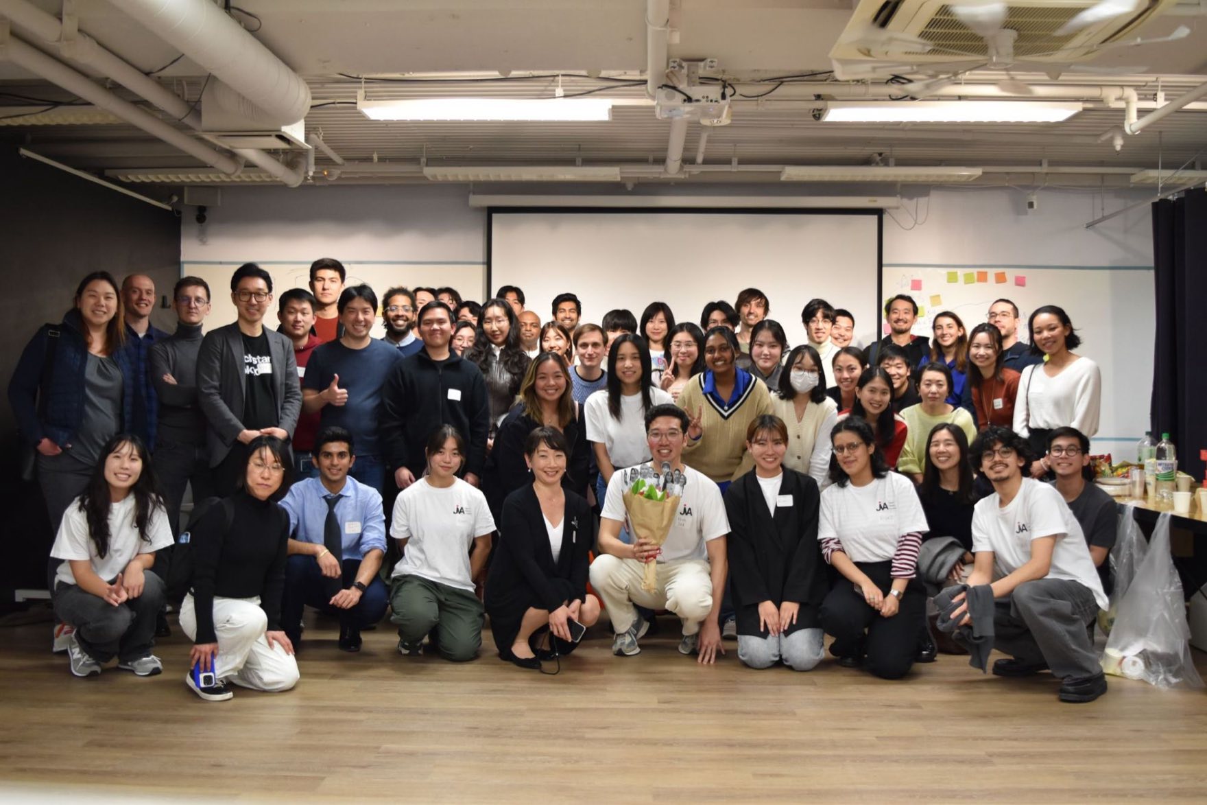 About forty JVA students and mentors posed together at the end of a cohort event in Tokyo, one holding a bouquet.